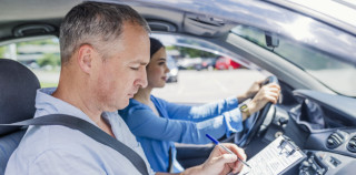 Instructor of driving school giving exam while sitting in car. Student driver taking driving test. Driving instructor and woman student in examination car IVA sulle patenti, UNASCA: batosta da 550 milioni