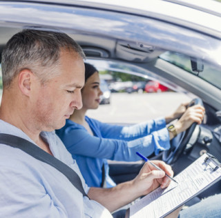 Instructor of driving school giving exam while sitting in car. Student driver taking driving test. Driving instructor and woman student in examination car IVA sulle patenti, UNASCA: batosta da 550 milioni